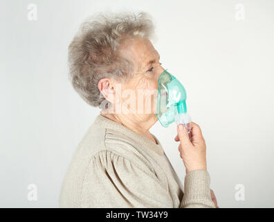 Elderly woman using asthma machine on light background Stock Photo