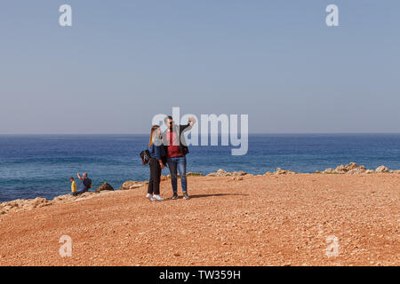 PAPHOS, CYPRUS - MAY 20, 2018: Young couple taking selfies on the rocky coast of Cyprus Stock Photo
