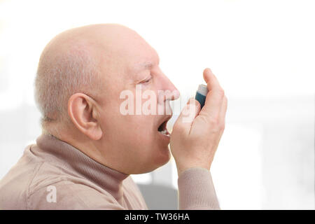 Senior man using asthma inhaler on light background Stock Photo
