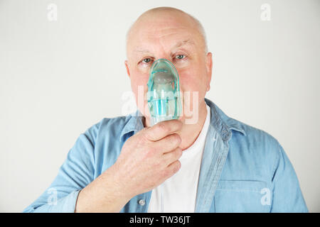 Senior man using asthma machine on light background Stock Photo