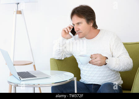 Mature man talking on phone and drinking tea in armchair Stock Photo