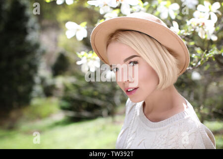 Young blonde girl in hat near blooming magnolia tree Stock Photo