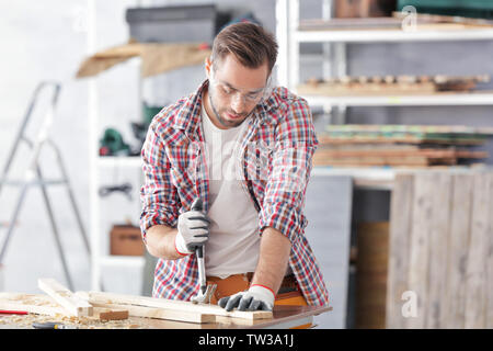 Carpenter pulling out nail from wooden plank in light workshop Stock Photo