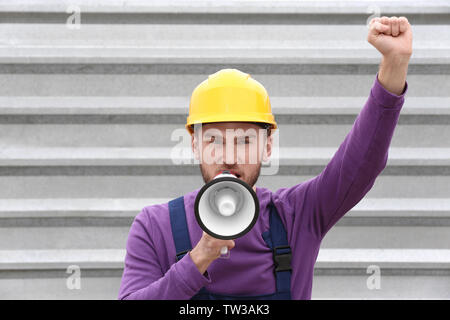 Protesting young man shouting into megaphone against metal fence Stock Photo