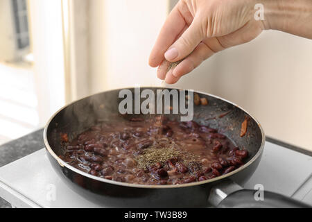 Female hand sprinkling herbs on beans in frying pan Stock Photo