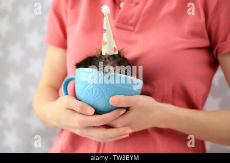 Young woman holding cup with cute rat in funny hat, closeup Stock Photo