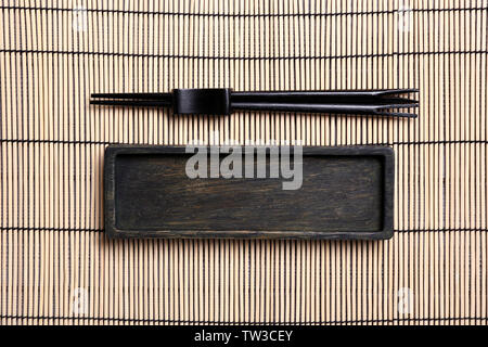 Empty rectangular wooden plate and chopsticks on bamboo mat Stock Photo