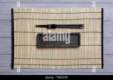 Empty rectangular wooden plate and chopsticks on bamboo mat Stock Photo