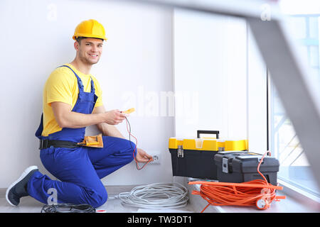 Electrician measuring voltage of socket indoors Stock Photo
