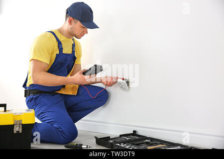 Electrician measuring voltage of socket indoors Stock Photo