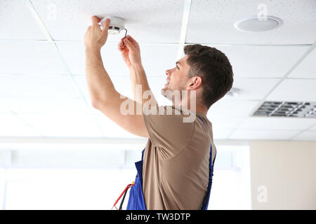 Young electrician installing smoke detector on ceiling Stock Photo