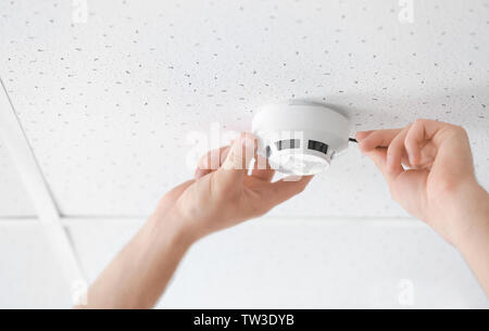 Electrician installing smoke detector on ceiling, closeup Stock Photo