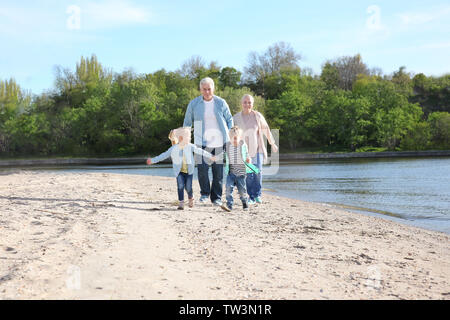 Happy grandparents playing with little children on river bank Stock Photo