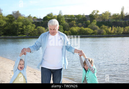 Happy grandfather playing with little children on river bank Stock Photo