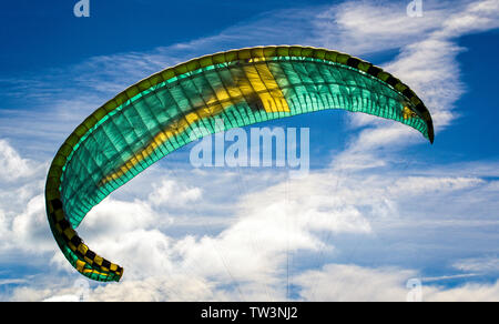 Green and yellow paragliding sail in the air against a blue sky backdrop Stock Photo