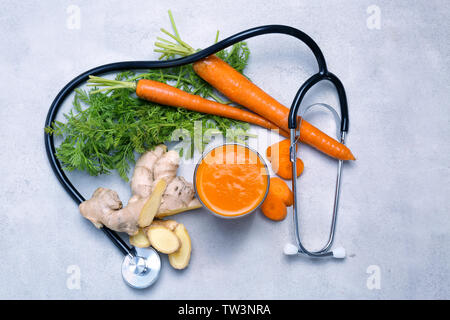 Glass of carrot juice with fresh ginger and stethoscope on grey background. Health care concept Stock Photo