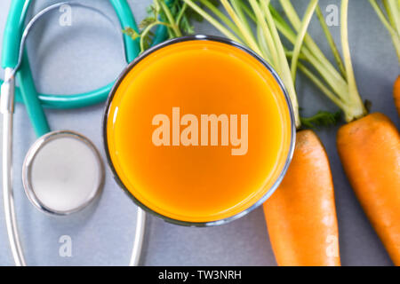 Glass of juice with fresh carrot and stethoscope on grey background. Health care concept Stock Photo