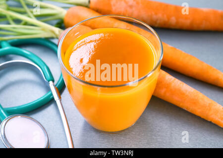 Glass of juice with fresh carrot and stethoscope on grey background. Health care concept Stock Photo