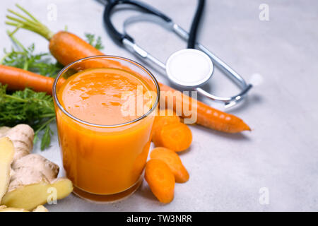 Glass of carrot juice with fresh ginger and stethoscope on grey background. Health care concept Stock Photo