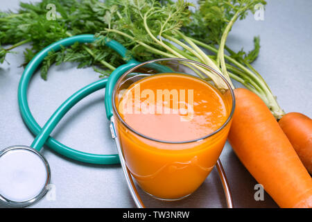 Glass of juice with fresh carrot and stethoscope on grey background. Health care concept Stock Photo