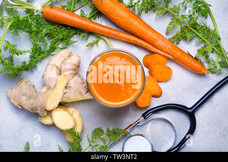 Glass of carrot juice with fresh ginger and stethoscope on grey background. Health care concept Stock Photo