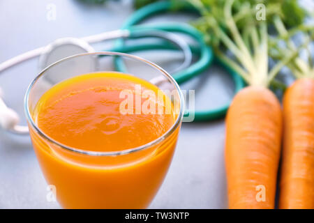 Glass of juice with fresh carrot and stethoscope on grey background. Health care concept Stock Photo