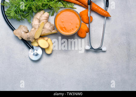 Glass of carrot juice with fresh ginger and stethoscope on grey background. Health care concept Stock Photo