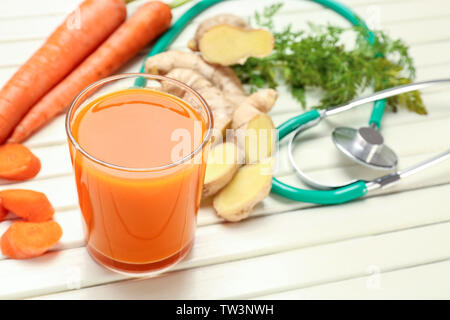 Glass of carrot juice with fresh ginger and stethoscope on white wooden background. Health care concept Stock Photo