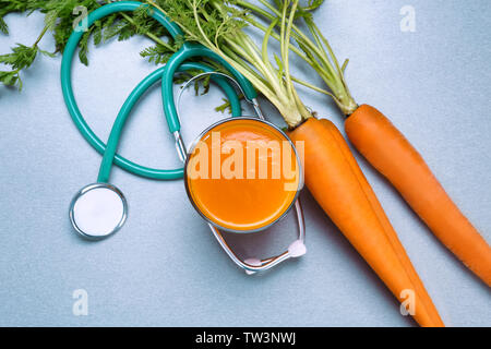 Glass of juice with fresh carrot and stethoscope on grey background. Health care concept Stock Photo