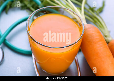 Glass of juice with fresh carrot and stethoscope on grey background. Health care concept Stock Photo