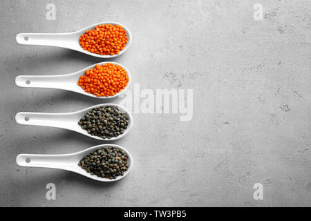 Ceramic spoons with black and red lentils on grey background Stock