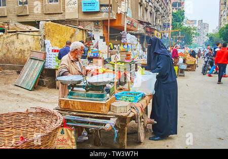 CAIRO, EGYPT - DECEMBER 22, 2017: The muslim woman, wared in black niqab and abaya, chooses fresh lemons and oranges in small stall of Souq As Sebaeyi Stock Photo