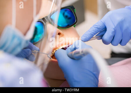 Dentist performing dental filling procedure to preteen girl in pediatric dental clinic. Doctor removing caries using high-speed dental drill. Child is Stock Photo