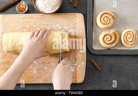 Woman cutting dough for cinnamon rolls on wooden board Stock Photo