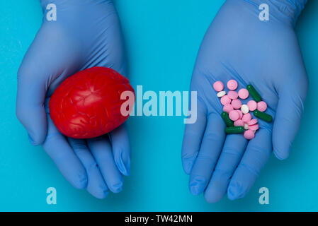 3D anatomical model of the brain and pink and blue pills on the palm on a blue background. Medical concept for a pharmacological pill for the treatmen Stock Photo