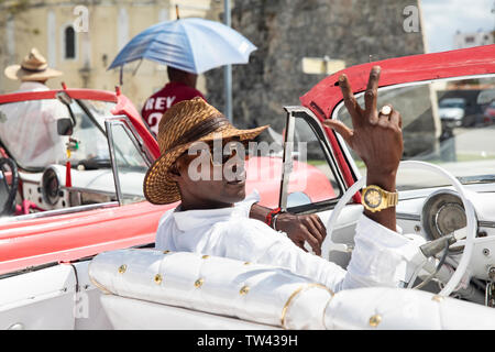 A Cuban taxi driver driving an old American car in Havana giving me the V’s sign. Stock Photo