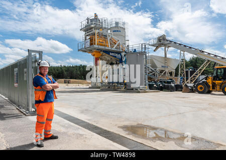 Workman in high visibility clothing standing by Meka Ready Mix Concrete Batching Plant for the production of concrete for the construction industry UK Stock Photo