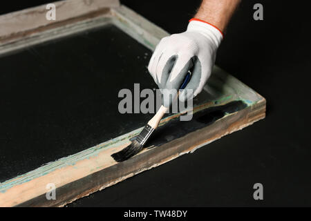 Hand of worker painting frame of old window, on dark background Stock Photo