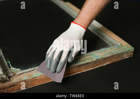 Hand of worker grinding surface of old window frame with abrasive paper, on dark background Stock Photo