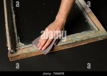 Hand of worker grinding surface of old window frame with abrasive paper, on dark background Stock Photo