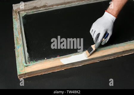 Hand of worker painting frame of old window, on dark background Stock Photo