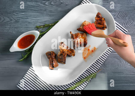 Woman adding sauce to roasted pork ribs in plate on wooden table Stock Photo