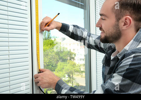 Young man installing window shades at home Stock Photo