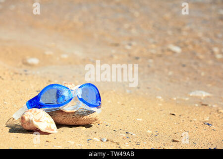 Swimming goggles, shells and stone on sand at sea shore. Vacation concept Stock Photo