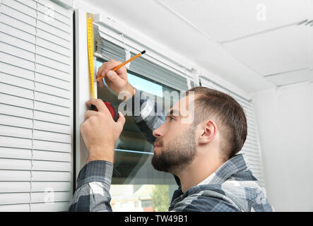 Young man installing window shades at home Stock Photo