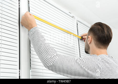 Young man installing window shades at home Stock Photo