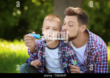 Dad and son blowing bubbles in the park on sunny day Stock Photo