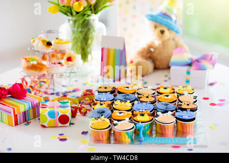 Cupcakes for kids birthday celebration. Jungle animals theme children party. Decorated room for boy or girl kid birthday. Table setting with presents, Stock Photo