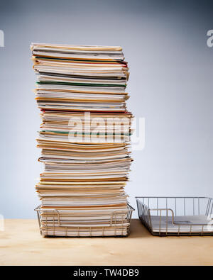 In, out trays on desk with tall stack of never ending office paperwork Stock Photo