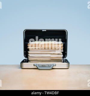 Overtime, tall stack of files and folders in aluminum briefcase. on light wood surface with blue background Stock Photo